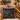 Decorative pillow with a scenic design on a wicker chair, with a poster of Valletta in the background.