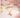 Gold unicorn necklace on a white surface with flowers and pink plush toys in the background
