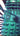 Teal Green Dalek pillow on a striped pillow with a wooden surface and decorative items in the background. Planet Retro NZ