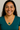 Woman wearing a teal shirt and gold necklace with a green paua pendant against a neutral background