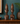 Two dark brown carved wooden bust sculptures with stylized faces and tall headdresses, displayed on a wooden cabinet against a teal wall with a plant and vase in the background.