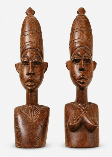 Two carved wooden bust sculptures with tall headdresses and stylized faces, shown side by side on a light gray background.