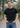 Man wearing a black t-shirt and blue jeans with a belt featuring a circular design outdoors.