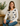 Woman wearing a white sweater with black bow patterns, sitting on a couch in a cozy room.