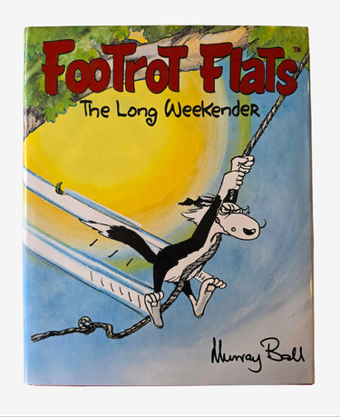 A hardcover book titled 'Footrot Flats: The Long Weekend' by Murray Ball, featuring a colorful cartoon illustration of a black and white dog on a swing against a yellow sun and blue sky, resting on a beige fabric surface.