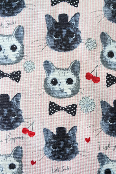 Close-up of KOKKA cats print with grey cat faces, pink pinstripes, bows, hearts and cherries