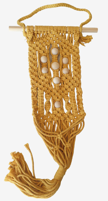 Mustard macramé wall plant holder with wooden beads hanging on neutral wall with small potted plant