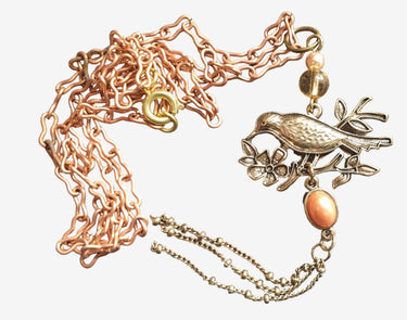 Bronze necklace with bird and floral pendant on a gray fabric background
