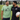 Two men standing on a grassy field, one wearing a green t-shirt with rugby-themed design and the other in an All Blacks sports shirt holding a rugby ball.