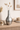 Silver vase with dried plants on a wooden surface with books and decor items.