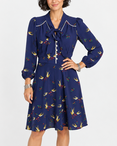 Female model wearing Trollied Dolly navy blue swallows print retro dress with pussy bow neckline and navy kitten heels, front view