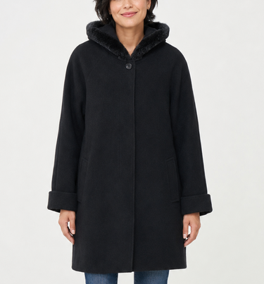 A woman modeling a black hooded coat with a fuzzy dark hood, paired with blue jeans and black ankle boots, against a plain light gray studio background.