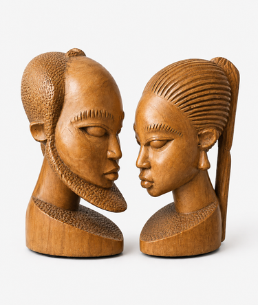 A pair of hand-carved wooden sculptures depicting two female busts facing each other, set against a plain light gray background.