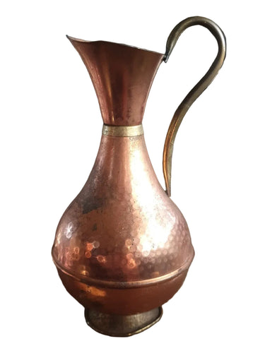 Vintage hammered copper jug with brass handle, showing warm metallic tones and textured decorative finish.