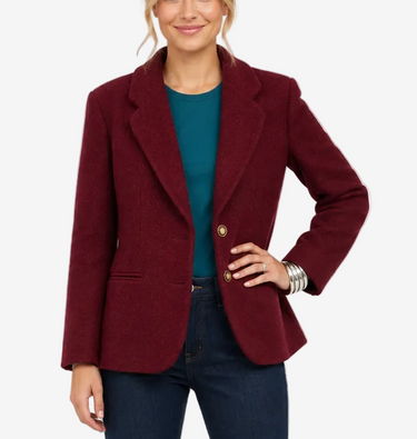 A woman modeling a tailored blazer in deep burgundy, worn over a teal top with dark blue jeans and burgundy heels, photographed against a clean white studio background.