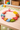 Colorful dinosaur-shaped toys on a wooden surface with a rainbow toy in the background.