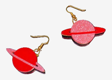 A pair of acrylic earrings designed to resemble the planet Saturn, with a gold-colored fixture and red and pink color scheme, displayed against a dark, starry background.