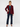 A woman modeling a tailored blazer in deep burgundy, worn over a teal top with dark blue jeans and burgundy heels, photographed against a clean white studio background.