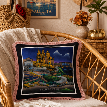 Decorative pillow with a scenic design on a wicker chair, with a poster of Valletta in the background.