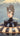 Vintage-style poster of a woman in a black cat suit inside a UFO with a mountain and trees in the background, displayed on a wooden surface with jewelry and sunglasses.  Planet Retro NZ