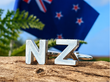 Silver 'NZ' cufflinks with New Zealand flag in the background