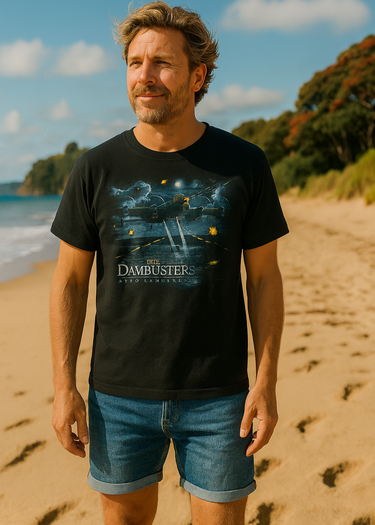 Man wearing a black t-shirt with 'Dambusters' design on a beach