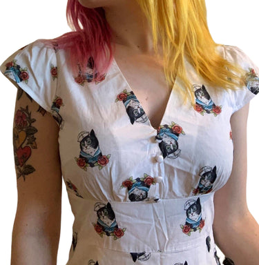 White dress with black cat and flower pattern worn by a person with tattoos and colorful hair.