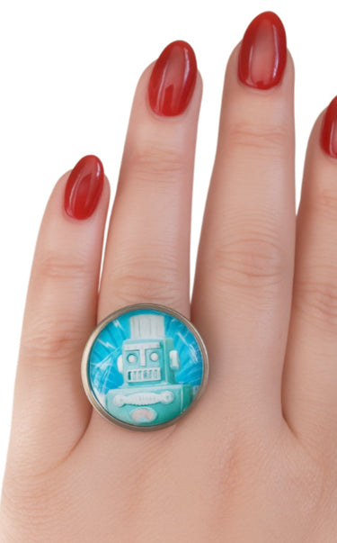 Ring with a blue and silver design on a hand with red nail polish against a white background