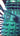 Teal Green Dalek pillow on a striped pillow with a wooden surface and decorative items in the background.  Planet Retro NZ