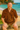 Man wearing a leopard print shirt sitting on a log by a beach.