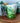 A white ceramic coffee mug with a green tropical plant pattern and a 3D toucan bird handle on a wooden surface, with a white flower in the background.