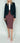 Person wearing a dark blazer, white shirt, maroon checkered skirt, and pink shoes on a plain background Planet Retro NZ