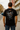Person wearing a black t-shirt with a graphic design on the back, standing on a street.