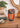 Decorative drum with orange and black design on a wooden surface, surrounded by plants and decor items.