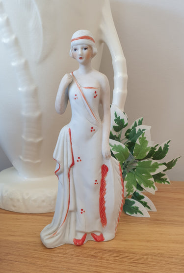Vintage-style ceramic figurine of a woman in a white dress with red accents on a wooden surface.  Planet Retro NZ.