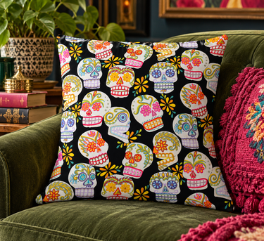 Black Sugar Skulls cushion cover styled on an olive-green velvet sofa with a magenta cushion, greenery and vintage books
