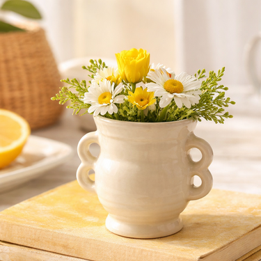 White ceramic vase with yellow and white flowers on a wooden surface