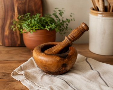 Wooden mortar and pestle on a cloth with a plant and container in the background