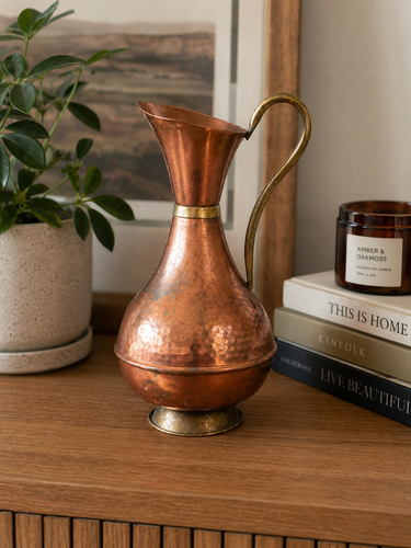 Vintage hammered copper jug with brass handle, showing warm metallic tones and textured decorative finish.