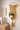 Yellow macrame wall hanging with a plant on a white wall above a wooden dresser.