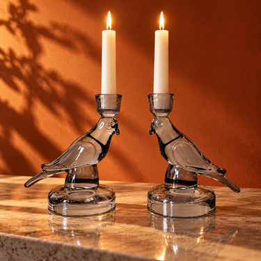 Pair of Nel Lusso smoky glass bird candle holders with lit ivory taper candles against a burnt orange wall