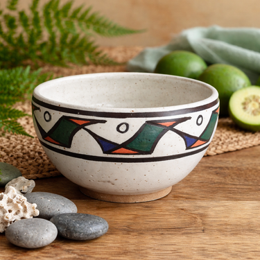 Ceramic bowl with decorative patterns on a wooden surface with limes and stones.
