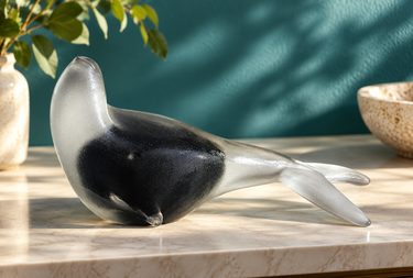 Nigel Schroders NZ studio glass seal displayed against teal wall with dappled light