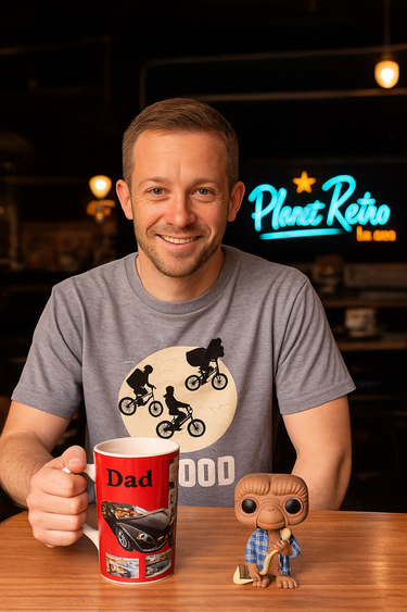 Man holding a mug with a 'Dad' design, sitting at a table with a 'Planet Retro' sign in the background.