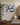 A square canvas wall art print featuring a monochrome painting of overlapping spheres, styled on a beige wall above a wooden table with a plant, books, a ceramic vase, and a lamp.