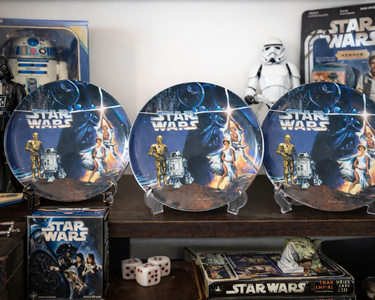 Three Star Wars-themed plates on a table with packaging and figures in the background.