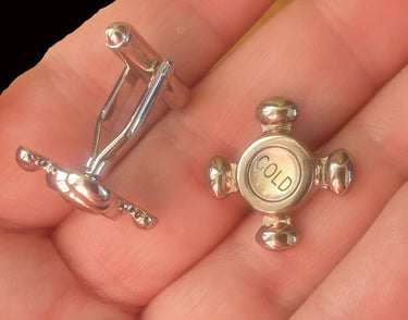 Small silver tap cufflinks with 'Cold' text held in a hand.