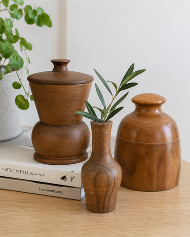 Set of three turned wooden vessels in warm brown timber tones, including two lidded pots and a small bud vase.