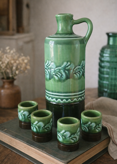 Green ceramic jug and cups on a wooden surface with a neutral background