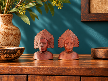 Pair of small vintage Balinese carved wooden busts styled on a wooden cabinet against a teal blue wall